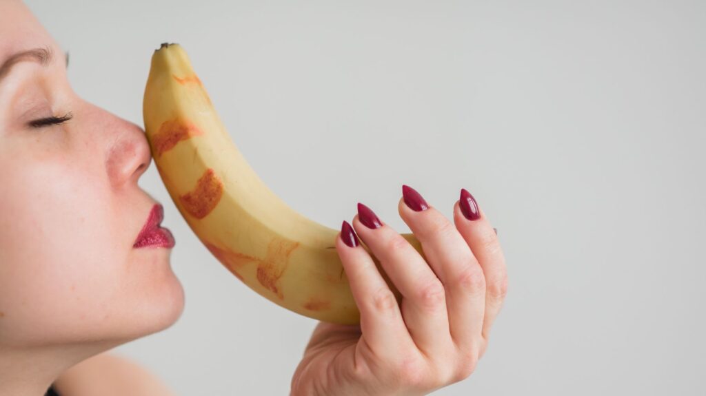 mulher segurando banana com beijos de batom para ilustrar um post sobre sexo oral