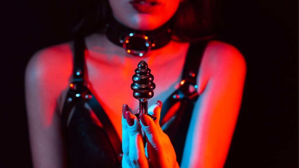 mulher com roupa para bdsm segurando um plug anal