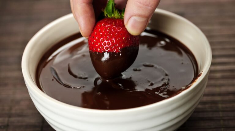 tigela com chocolate e mão segurando um morango para usar comida no sexo
