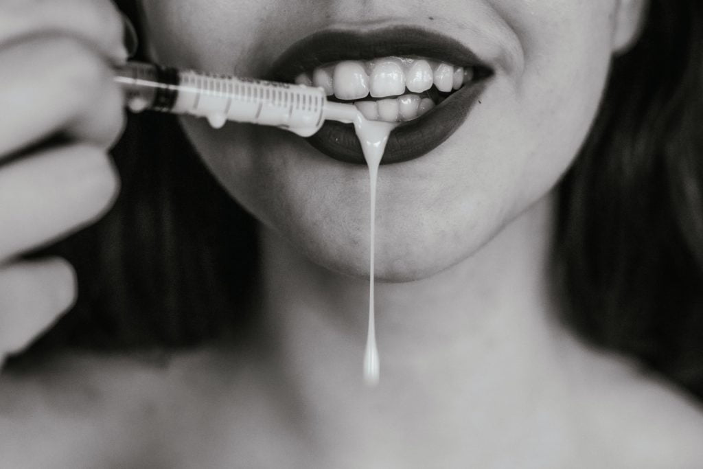 Mulher derrama um gel comestível nos lábios. Imagem disponível em Unsplash.