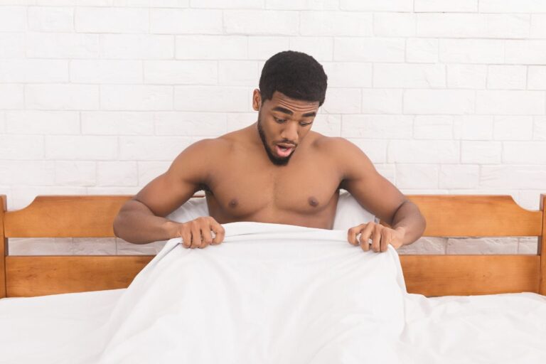 homem na cama com lençol olhando para o pênis