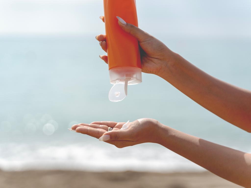 mãos de mulher segurando protetor solar e colocando uma quantia na palma