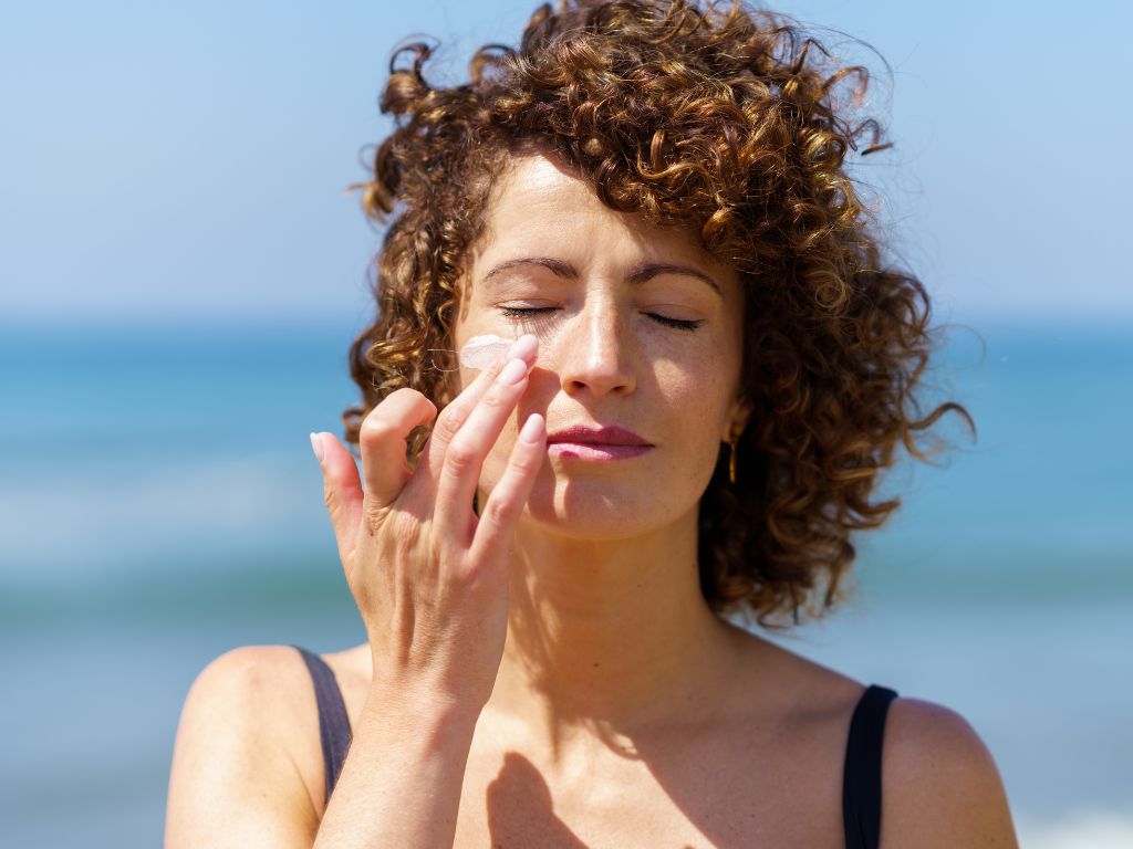 mulher de cabelo cacheado passando protetor solar na praia