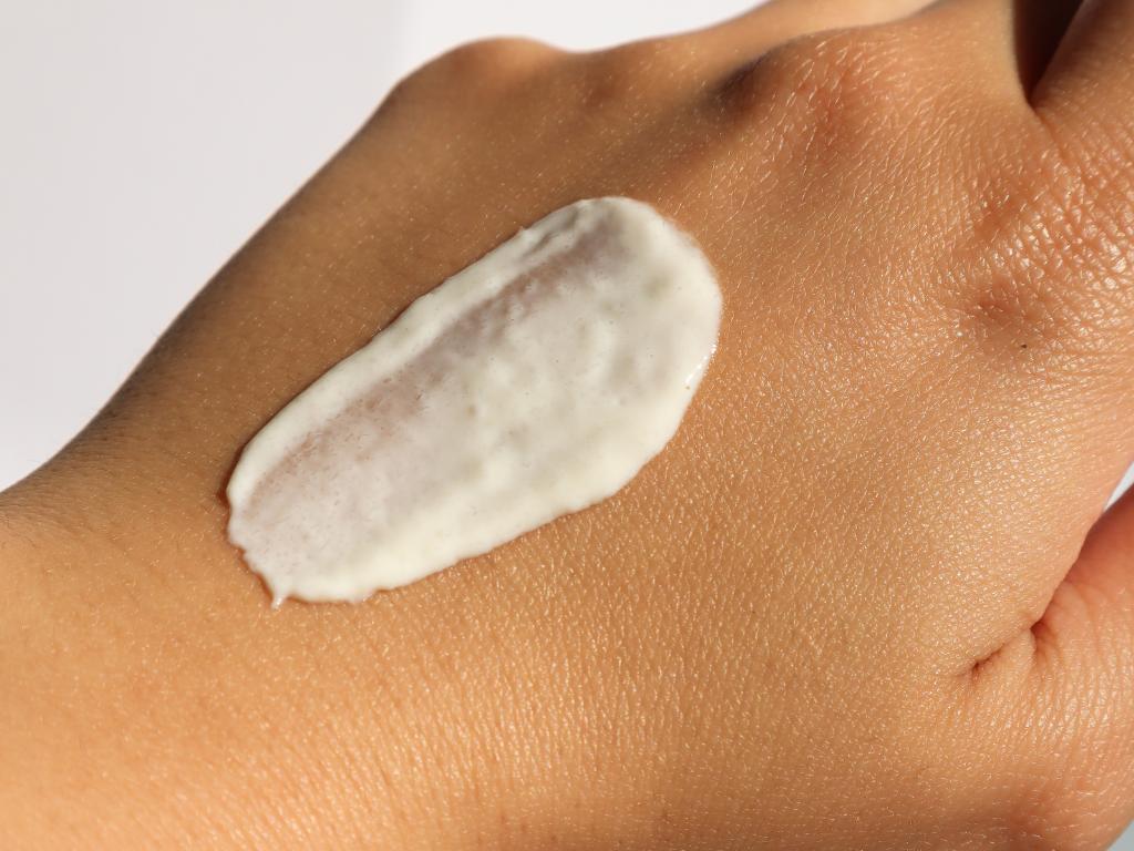 close de uma mão com um pouco de protetor solar espalhado, mostrando a textura do protetor