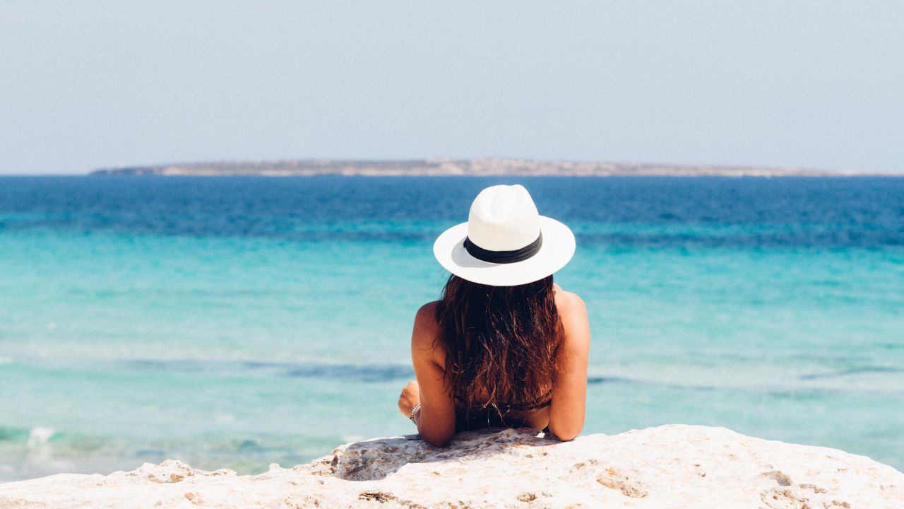 mulher deitada na areia de costas com chapéu em uma praia brasileira