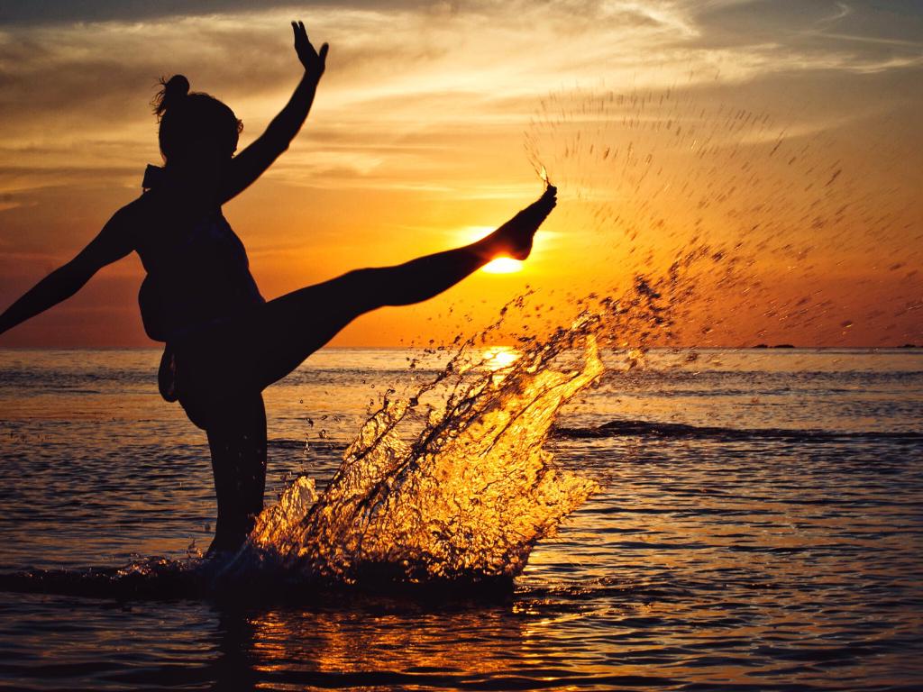 mulher com uma perna para cima brincando com a água no mar durante o por do sol
