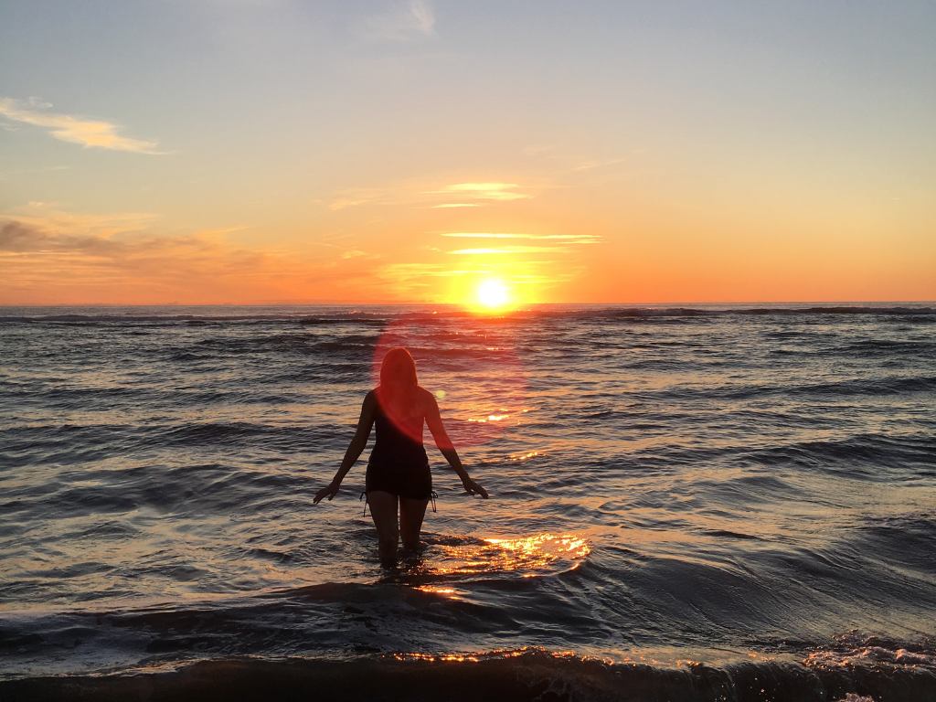mulher andando no mar ao entardecer