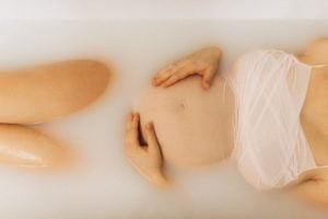 Mulher grávida em uma banheira com água branca.