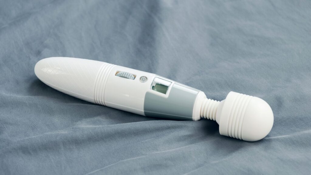 vibrador varinha mágica branco e cinza em cima de lençol cinza