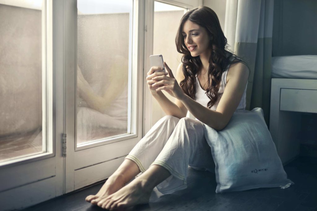 Mulher sentada na janela com um celular na mão.