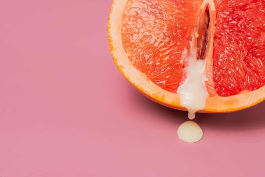 Metade de uma laranja com um líquido branco escorrendo, em um fundo rosa.