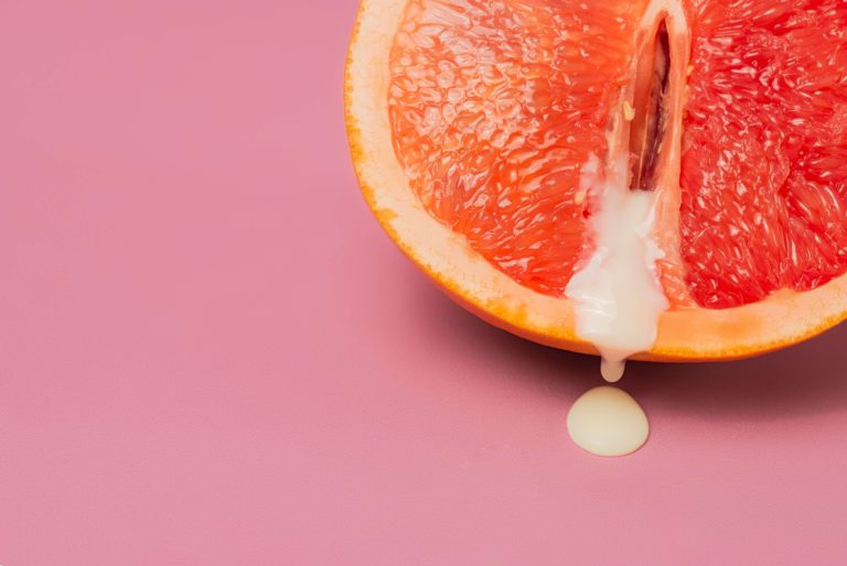 Metade de uma laranja com um líquido branco escorrendo, em um fundo rosa.