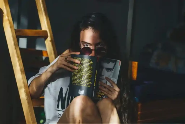 Mulher lê um livro sentada e olhando discretamente. Imagem disponível em Unsplash.