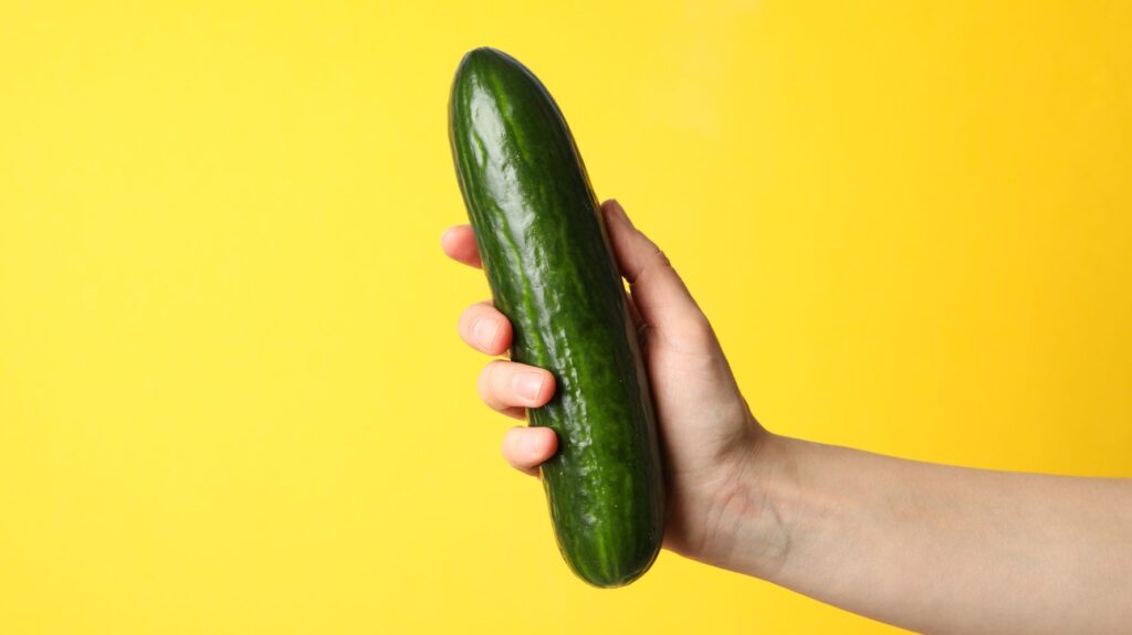 mão segurando pepino para remeter a pênis bem firme