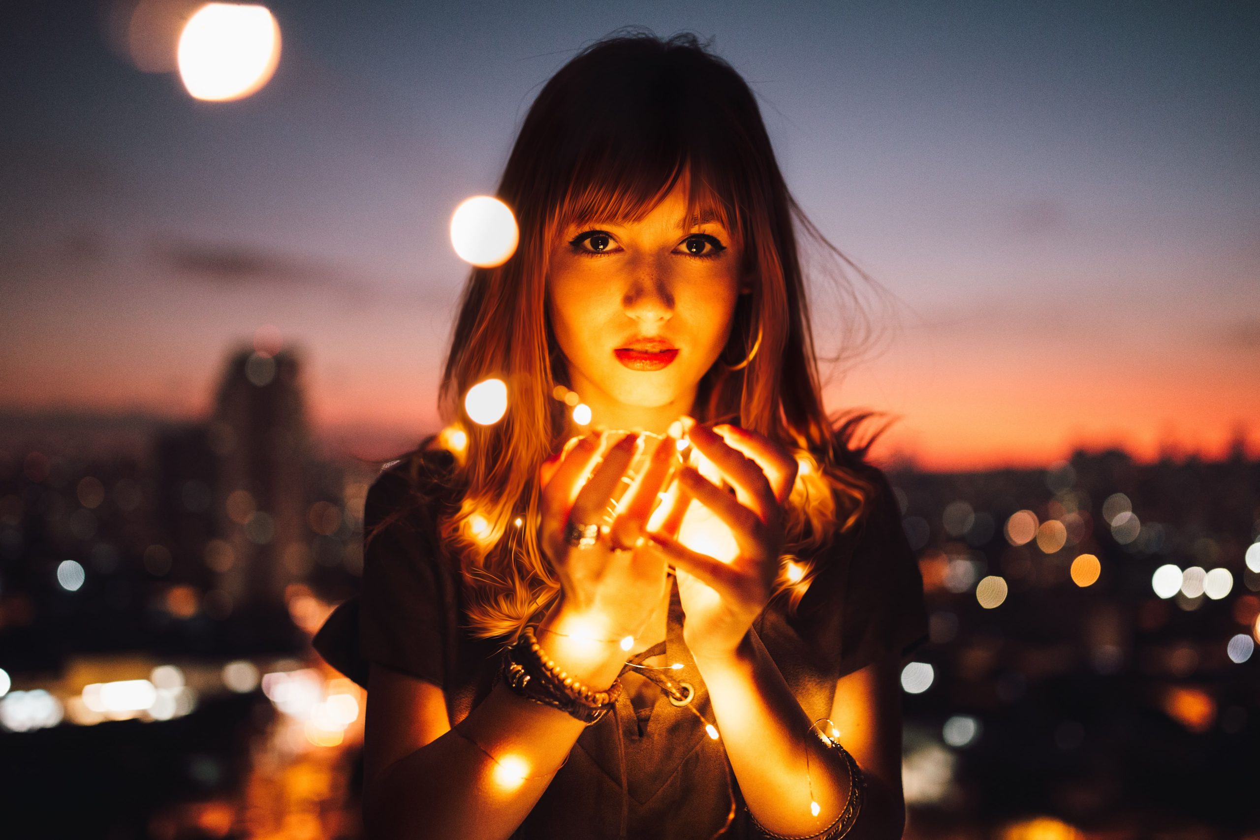 Mulher segurando pequenas lâmpadas que iluminam suas mãos e rosto.