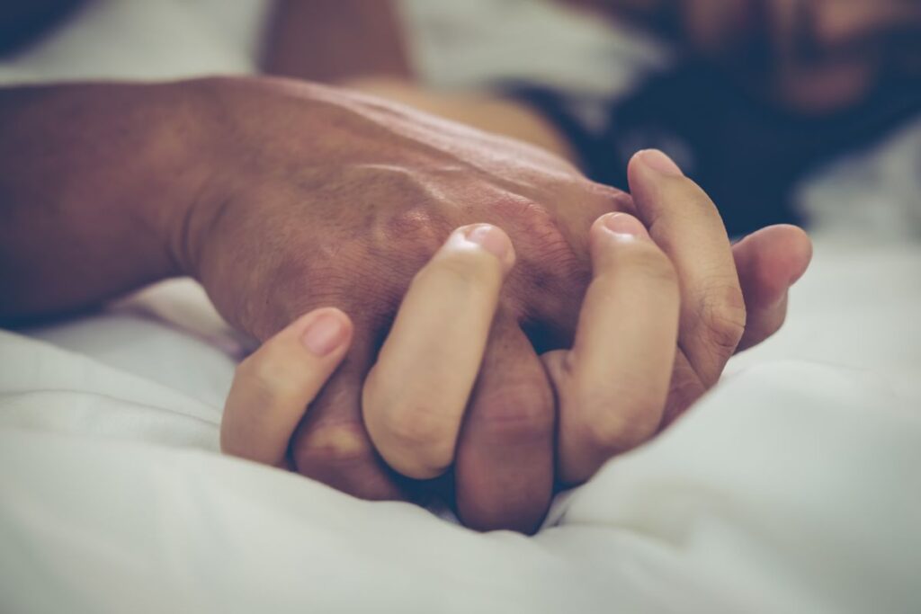 casal na cama com as mãos entrelaçadas