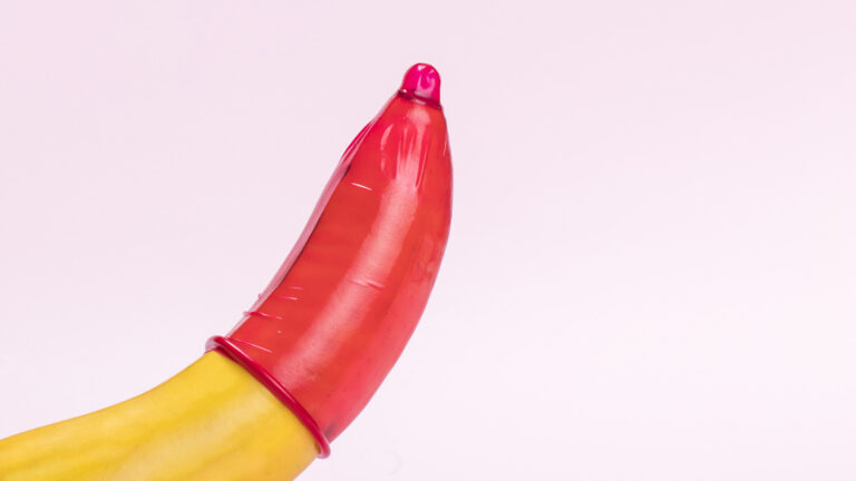 Camisinha vermelha colocada em uma banana diante de um fundo rosa.