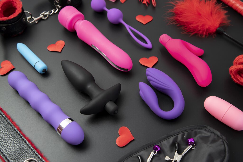 Diversos vibradores e outros produtos de sex shop colocados sobre uma mesa, com diferentes cores e modelos.
