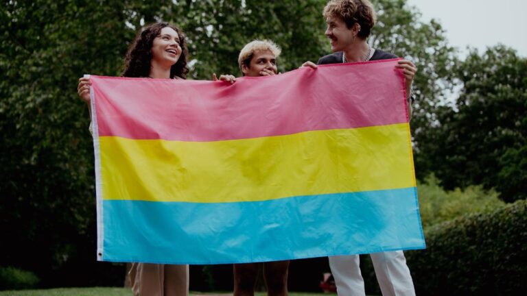 Três pessoas segurando bandeira que representa a pansexualidade.