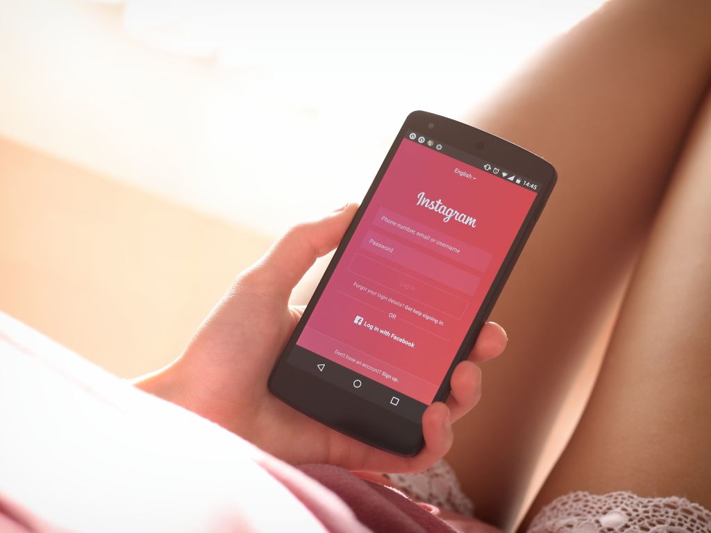 mulher de pijama com um celular na mão na página de loggin do instagram