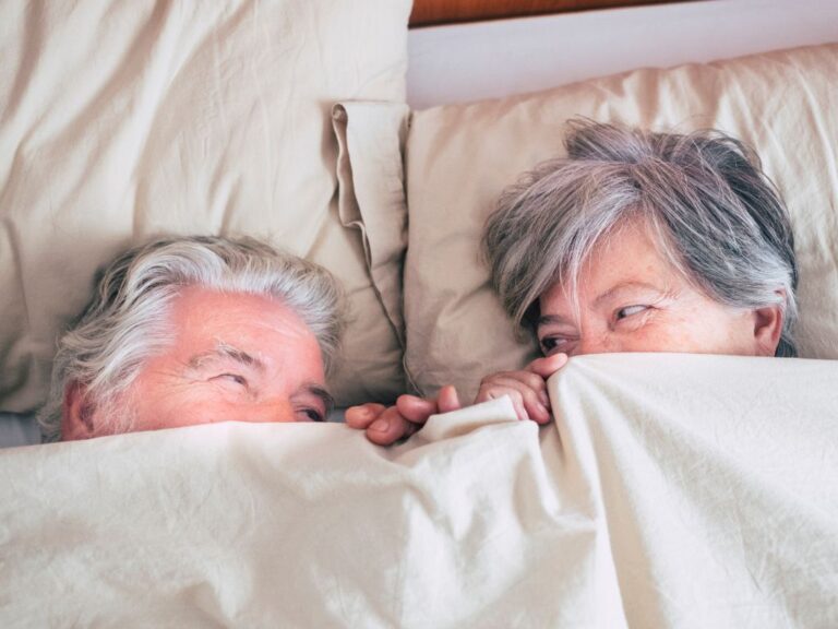 casal de idosos na cama com lençol até a altura dos olhos