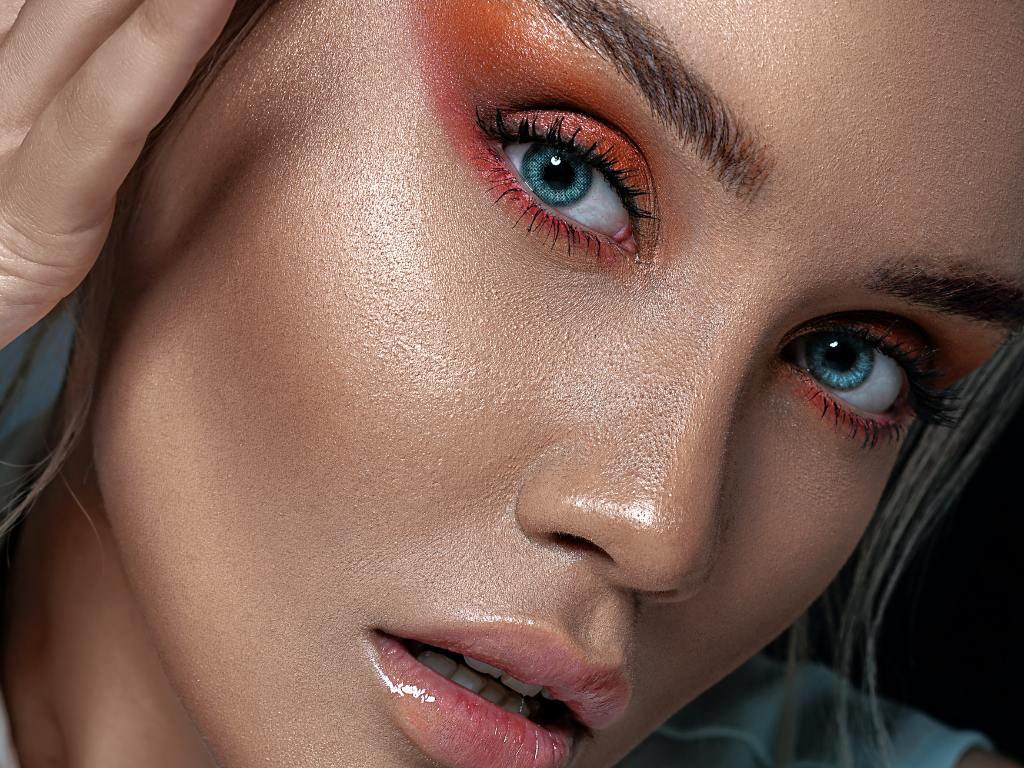 Mulher usando maquiagem com efeito glow e tons de vermelho e laranja