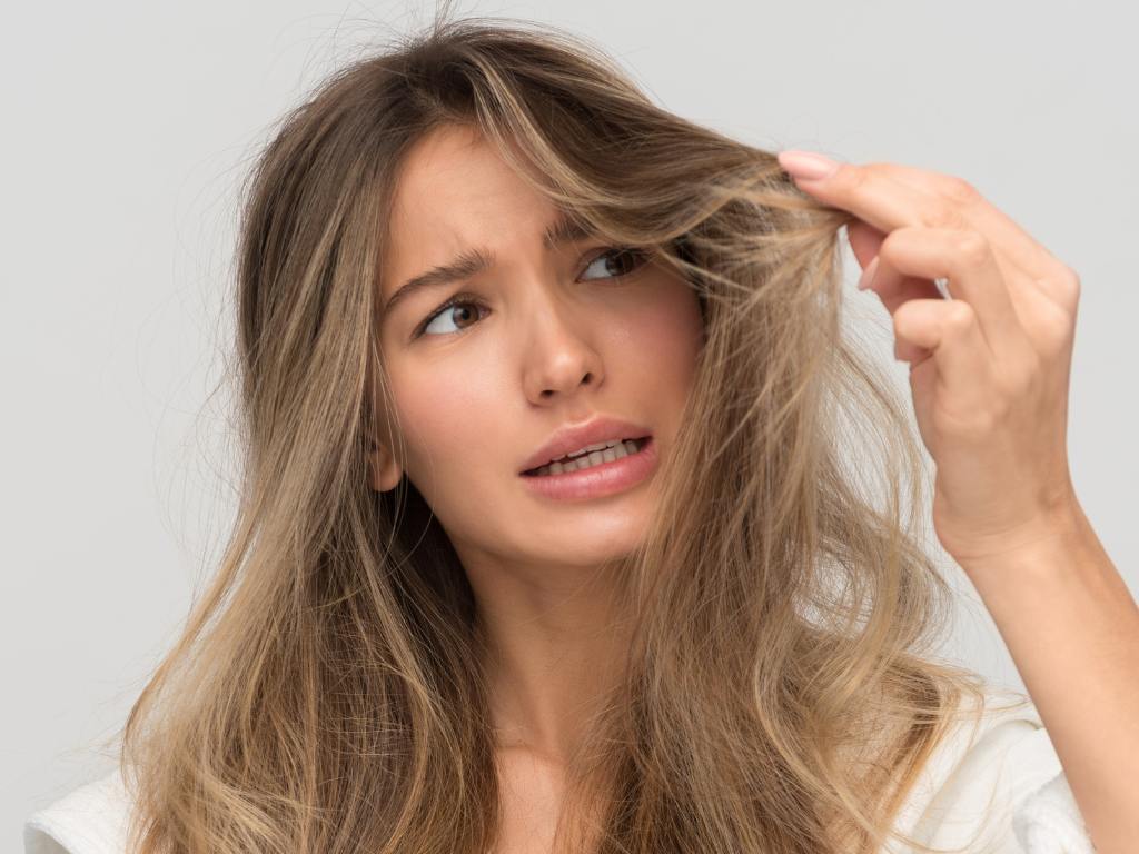 Mulher loira olhando cabelo desidratado