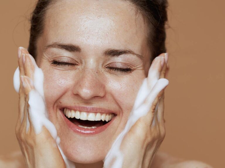 Mulher sorrindo ao aplicar sabonete facial