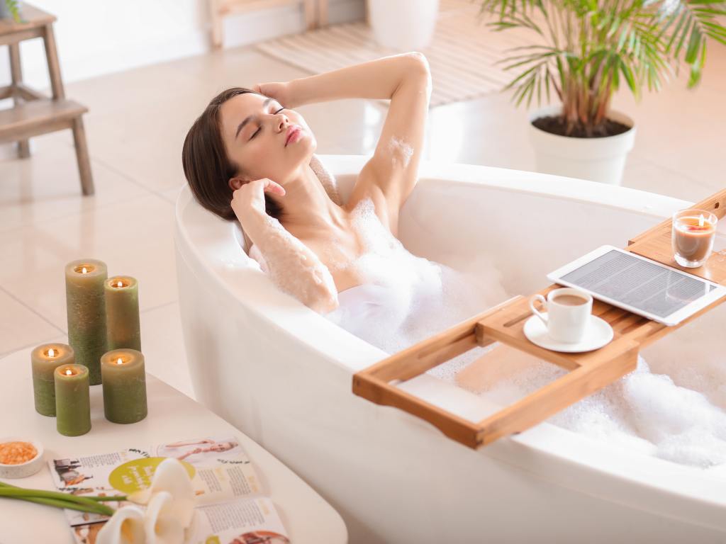Mulher tomando banho premium com velas, comida e tablet na banheira