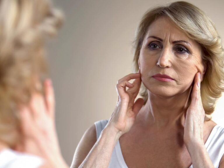 Mulher se olhando no espelho e vendo seus sinais de envelhecimento