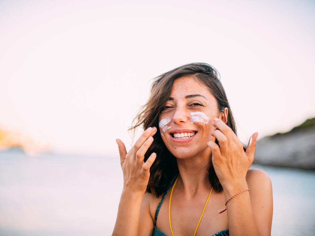 Mulher sorrindo e aplicando protetor solar no rosto