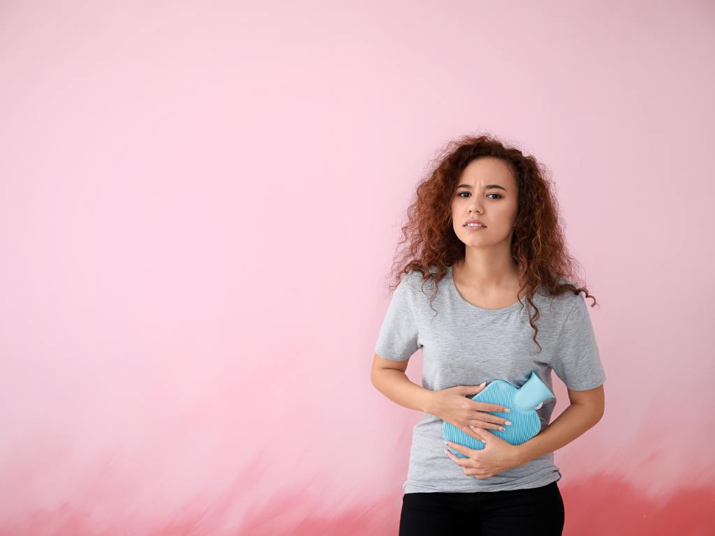 Mulher com dores no ovário usando bolsa de água quente para aliviar sua dor