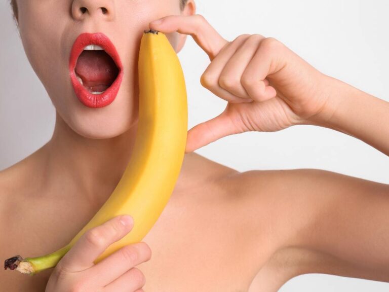 Mulher segurando uma banana perto da boca