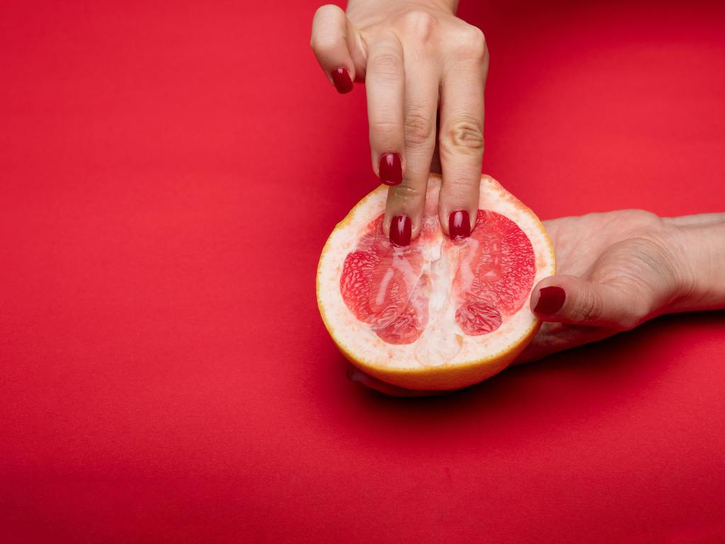 mulher tocando uma laranja aberta para representar uma vagina