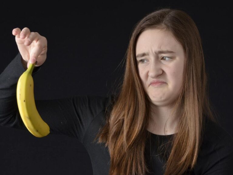 Mulher segurando banana com cara de nojo