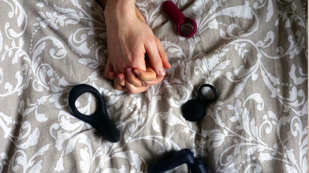 mãos de casal entrelaçadas com brinquedos sexuais ao redor