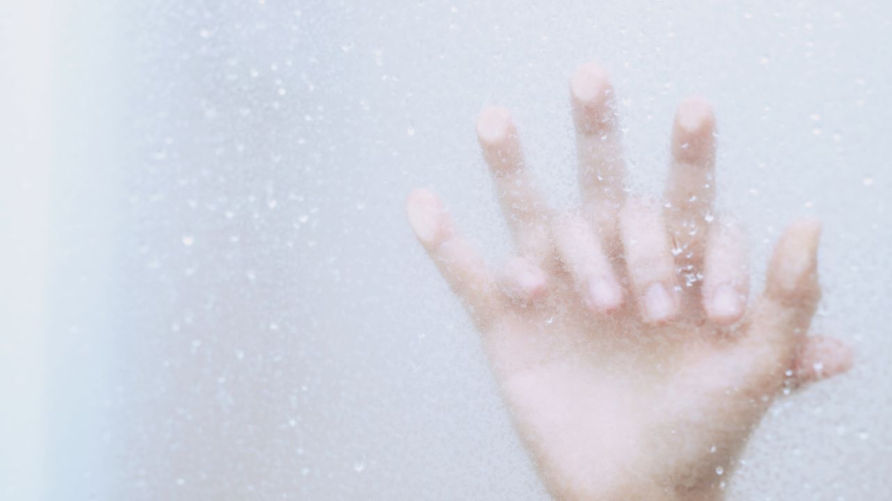 mãos de casal entrelaçadas no box do chuveiro molhado