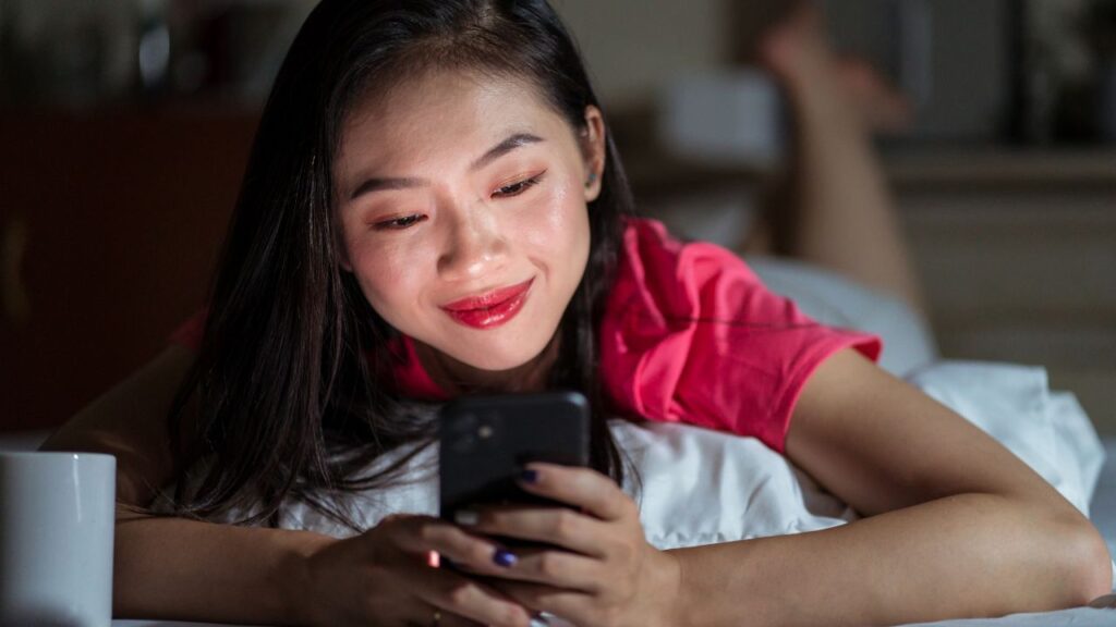 mulher deitada na cama com celular na mão usando hinge