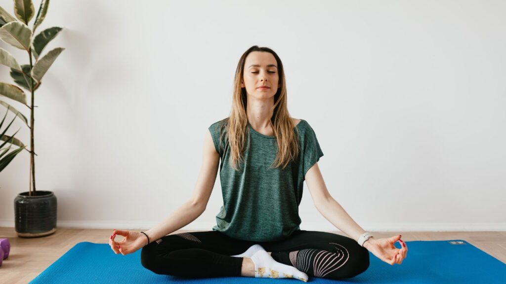 mulher loira sentada em um tapetinho azul fazendo yoga