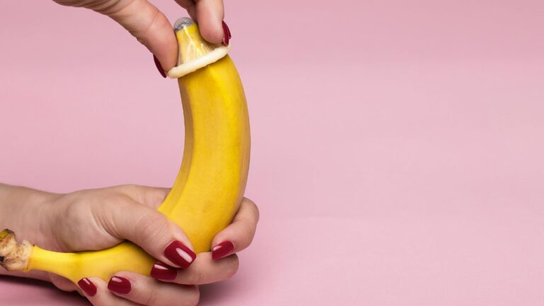 mão colocando camisinha na banana representando pênis