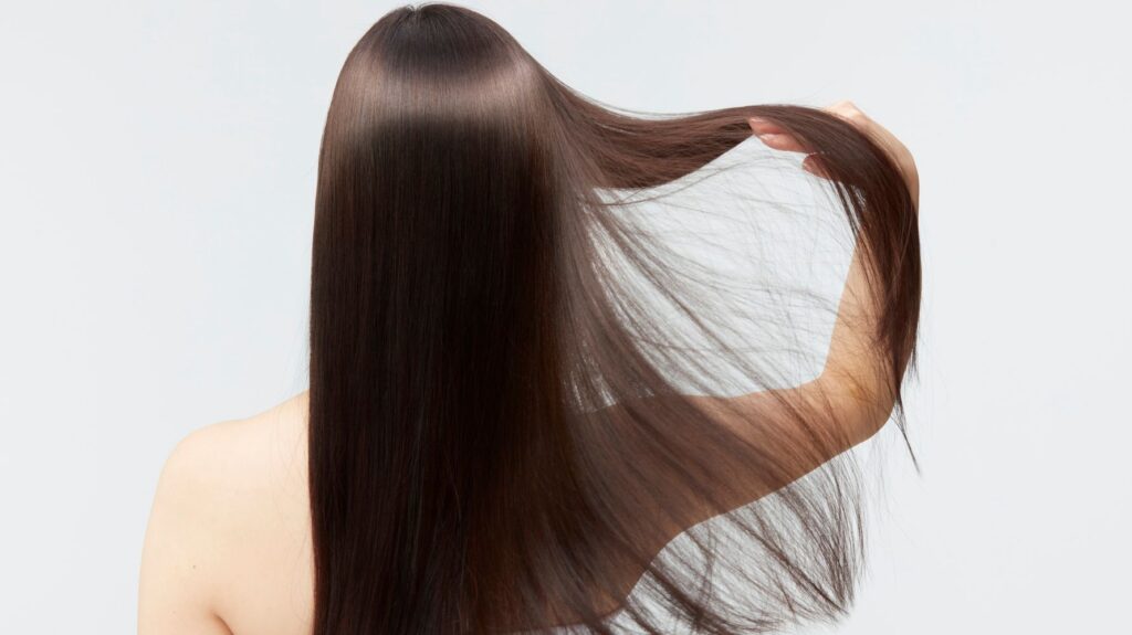 mulher de costas com cabelo liso e brilhoso espalhando o cabelo com uma das mãos