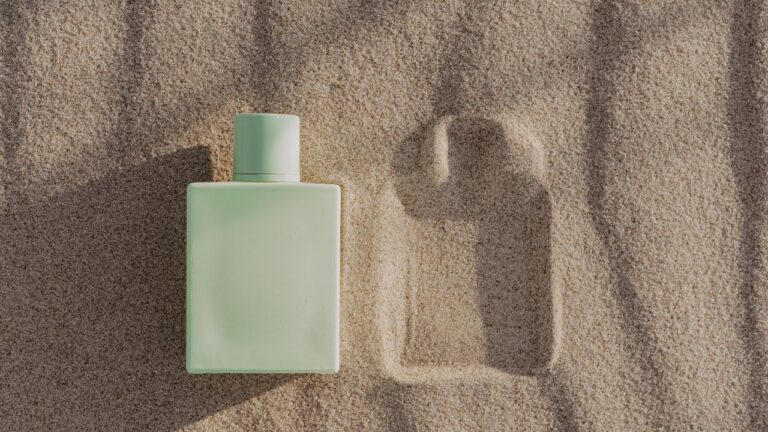frasco verde de perfume fresco na areia de praia