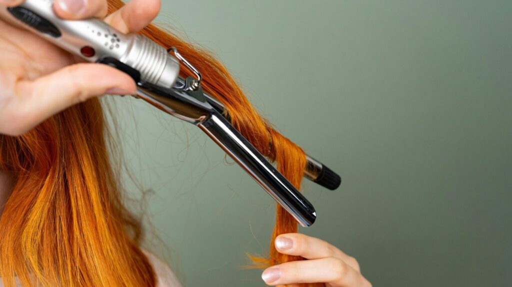 cabelo ruivo sendo enrolado em babyliss em fundo verde
