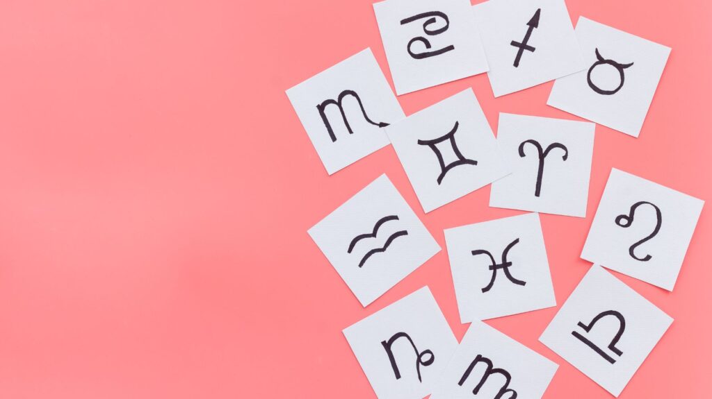 papeis brancos com simbolos de signos em fundo rosa