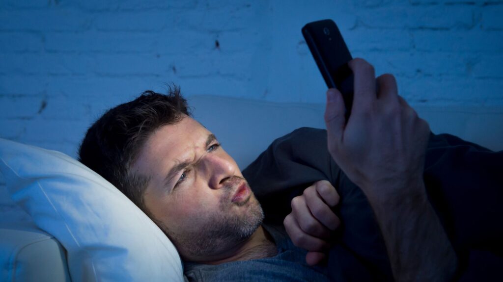 homem deitado na cama com celular na mão com vício em pornografia