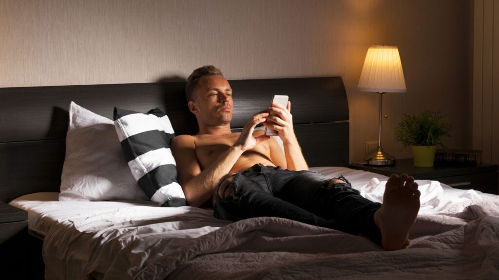 homem sem camisa na cama usando celular